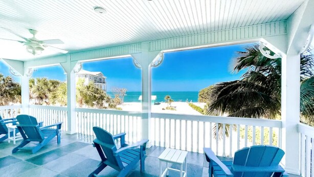 A covered outdoor area with blue Adirondack chairs and a small table, overlooking a beach and ocean.