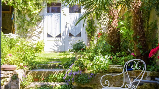 A garden with a white bench, stone steps, and a white building with windows in the background. - Gorgeous home in Saint-Martin-de-Ré with WiFi (Saint-Martin-de-Ré)