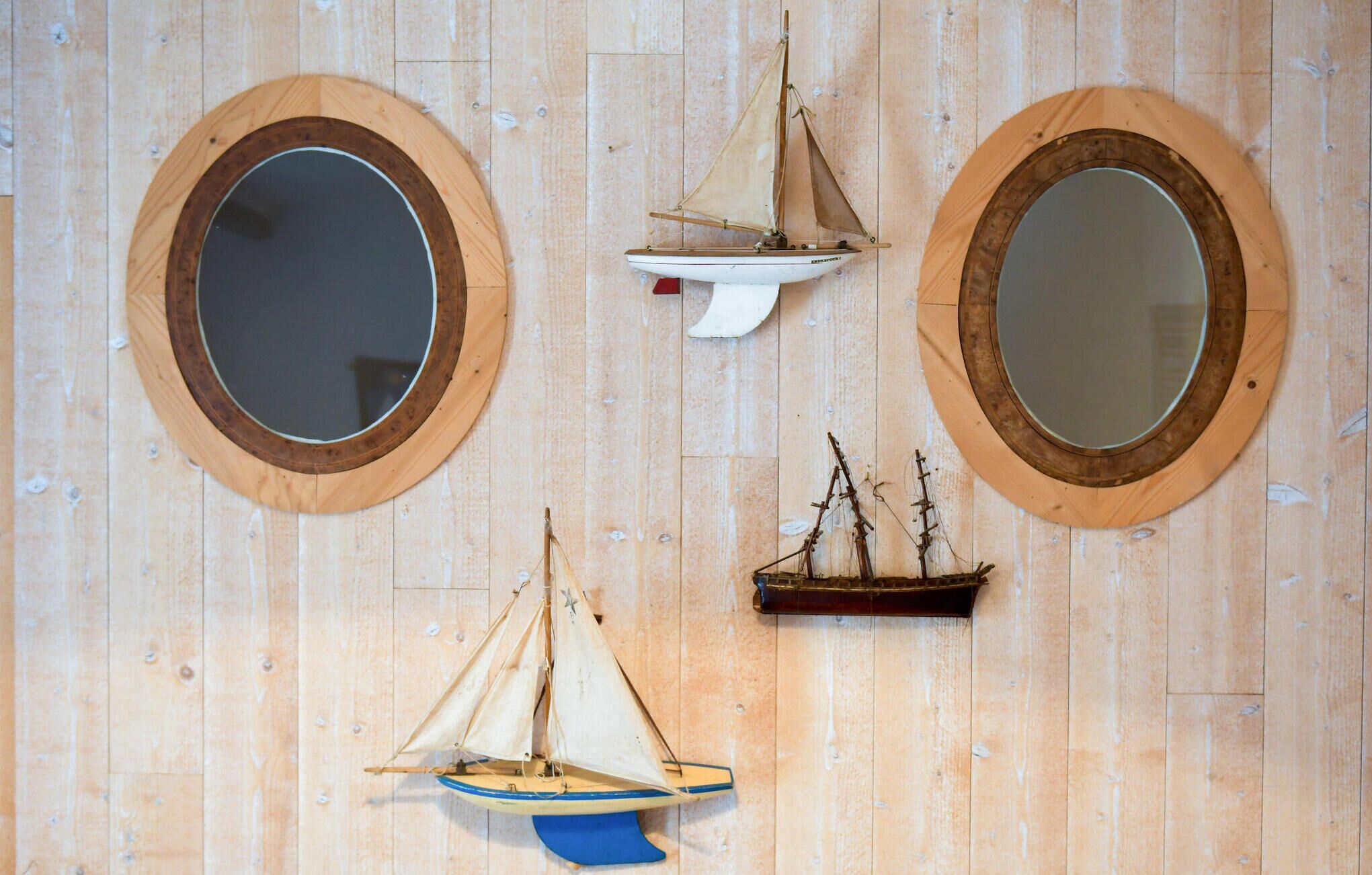A wooden wall with three circular mirrors and two model ships.