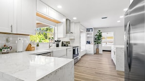 A modern kitchen with white cabinetry, a large island, and a stainless steel refrigerator. - Stunning Retreat - Hot Tub - Sauna - Heated Pool - Games Room- Cold Plunge (Palm Beach Gardens)