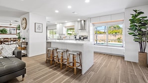 A modern kitchen with a central island, bar stools, and a dining area with a sofa and table. - Stunning Retreat - Hot Tub - Sauna - Heated Pool - Games Room- Cold Plunge (Palm Beach Gardens)