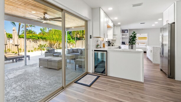 A modern kitchen with a central island, white cabinetry, and a view of the outdoor patio area. - Stunning Retreat - Hot Tub - Sauna - Heated Pool - Games Room- Cold Plunge (Palm Beach Gardens)