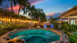 A hot tub surrounded by a wooden fence, palm trees, and a building with outdoor seating. - Stunning Retreat - Hot Tub - Sauna - Heated Pool - Games Room- Cold Plunge (Palm Beach Gardens)