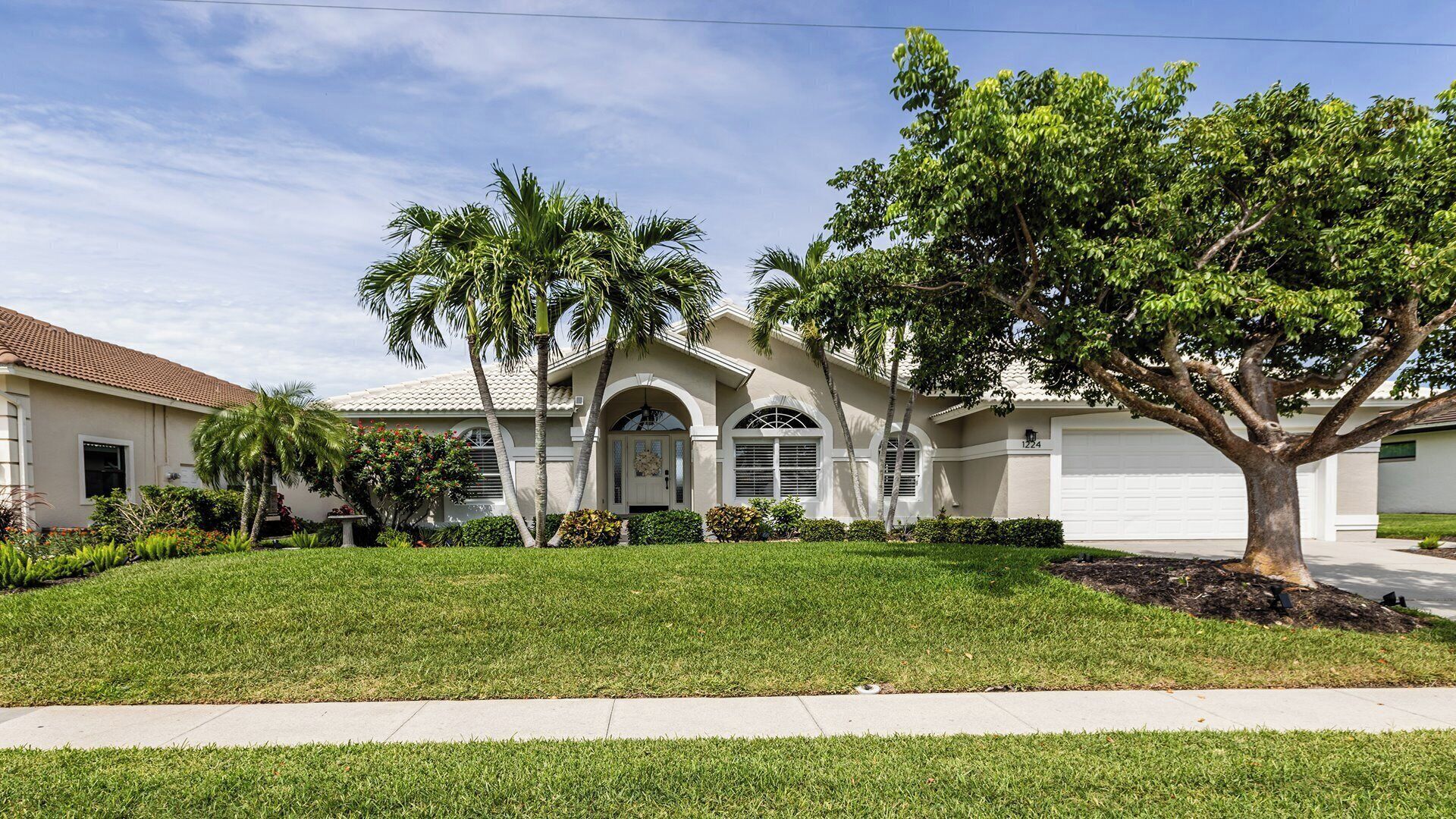 A residential house with a well-maintained lawn, a driveway, and a large tree in the front yard.