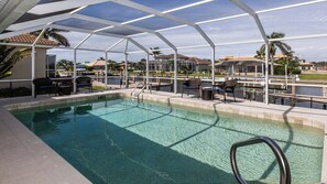 A pool area with clear water, surrounded by a covered patio with chairs and tables. - Modern, sleek and chic are only a few words to describe this home. (Marco Island)