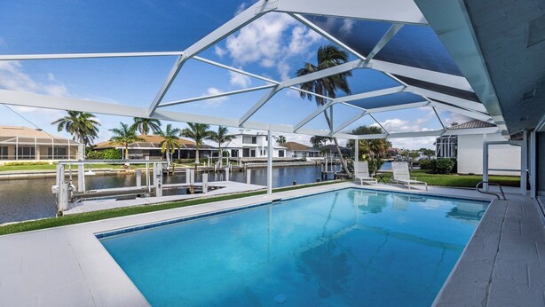 Une piscine offrant une vue dégagée sur l’eau, entourée d’une terrasse blanche et d’un espace abrité doté d’une structure de toit aux lignes géométriques.