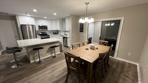 A modern kitchen with white cabinets, stainless steel appliances, and a wooden dining table with four chairs. - Get Cozy in this newly renovated home by The Villages! (Lady Lake)