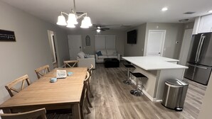 A modern kitchen with a wooden dining table, bar stools, and a stainless steel refrigerator. - Get Cozy in this newly renovated home by The Villages! (Lady Lake)
