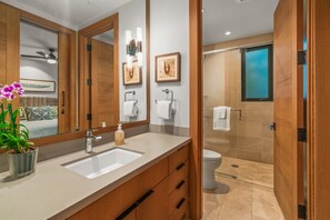 A modern bathroom with a large mirror, wooden cabinets, a sink, and a shower area. - Malu Makani by Alekona Kauai: 2 BR Luxury Oceanview Kukuiula Condo w private pool, AC, large lanai (Koloa)