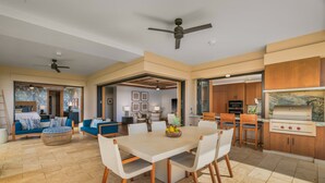 Un grand espace de vie comprenant un coin repas avec table et chaises, des canapés et un coin cuisine équipé d’un barbecue.