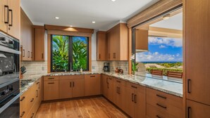 Une cuisine moderne avec des meubles en bois, une grande fenêtre donnant sur un paysage verdoyant et le ciel, et un four encastré.