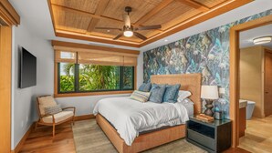 Une chambre avec un grand lit, un ventilateur de plafond, une fenêtre donnant sur un paysage verdoyant et une table de chevet avec une lampe.