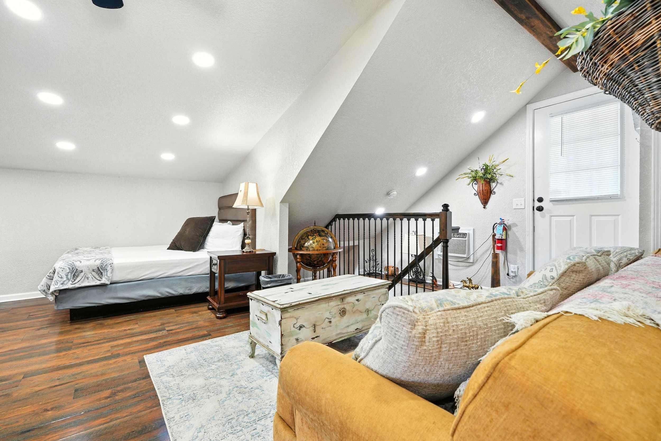 A bedroom with a bed, bedside table, lamp, dresser, and a staircase leading to another room.