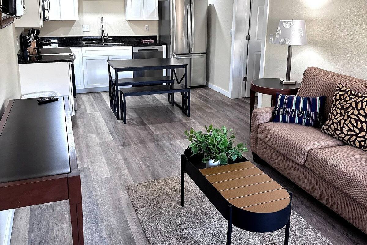 A modern living room with a sofa, coffee table, and a dining area with a kitchen in the background.