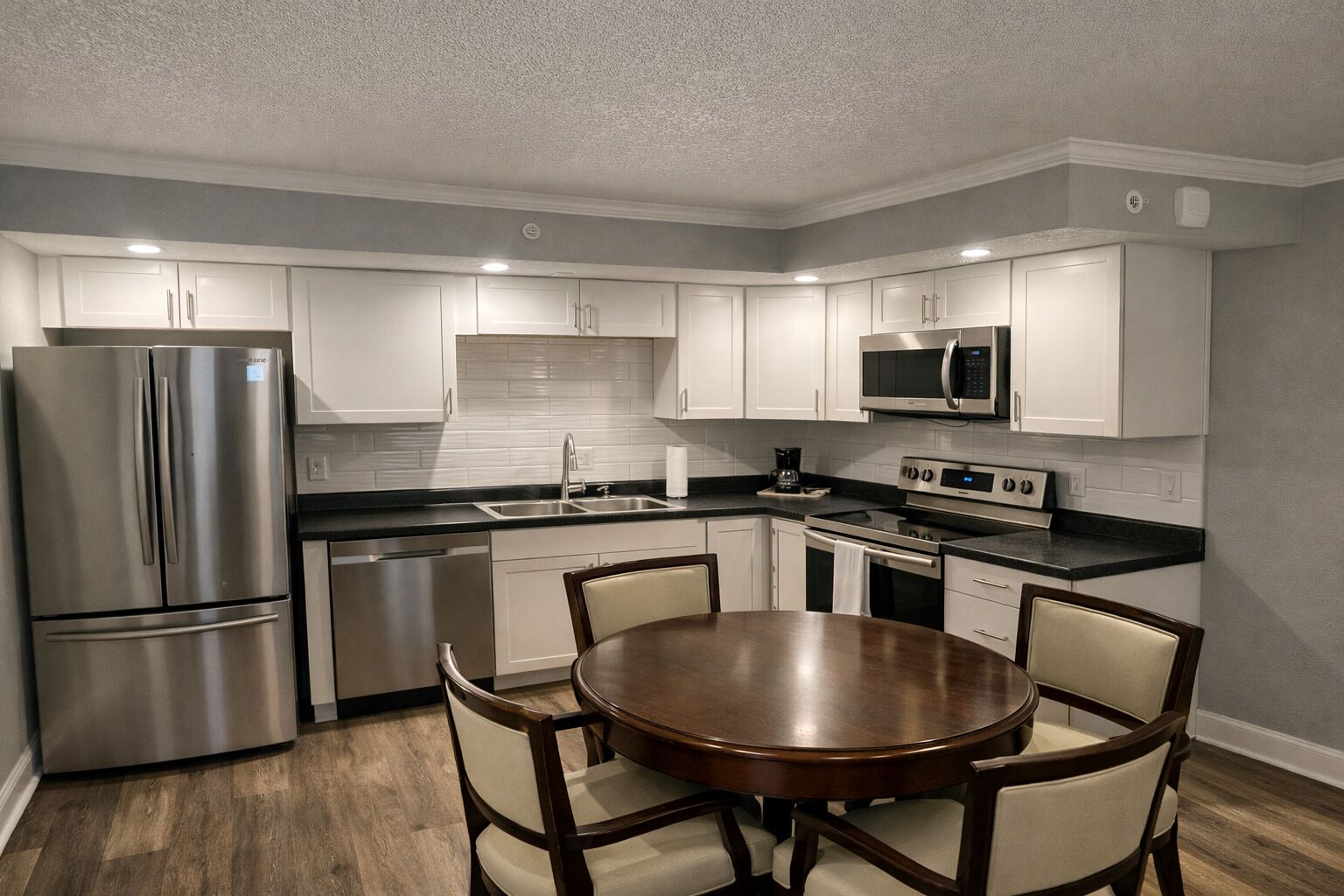 A modern kitchen with white cabinets, stainless steel appliances, a round dining table, and four chairs.