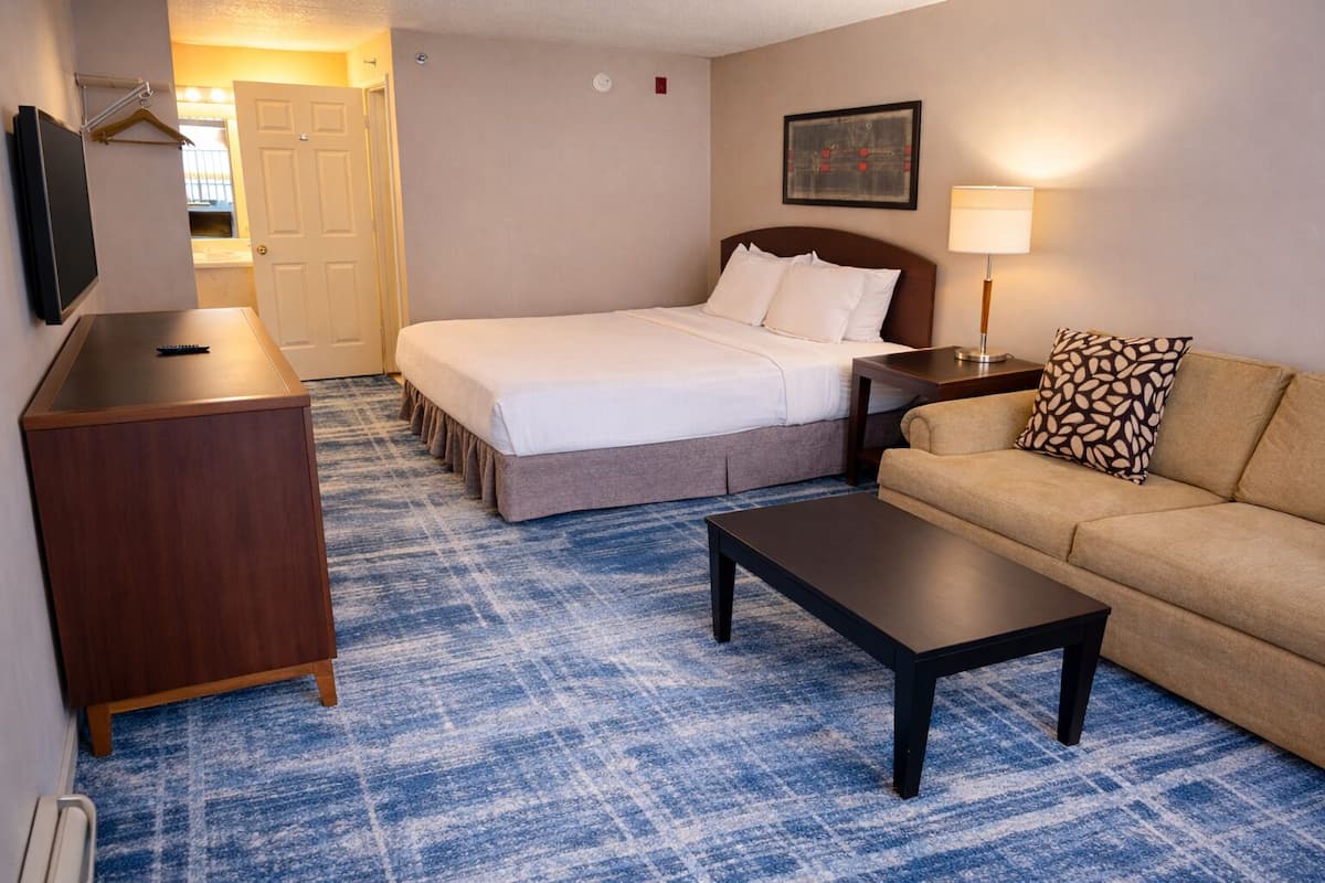 A hotel room with a bed, a sofa, a coffee table, a TV, and a desk.