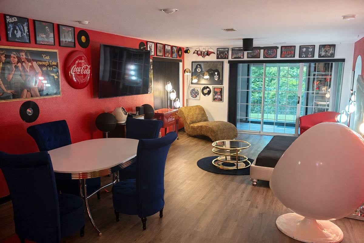 A modern living room with a red accent wall, a flat-screen TV, a round coffee table, and a large pink spherical chair.