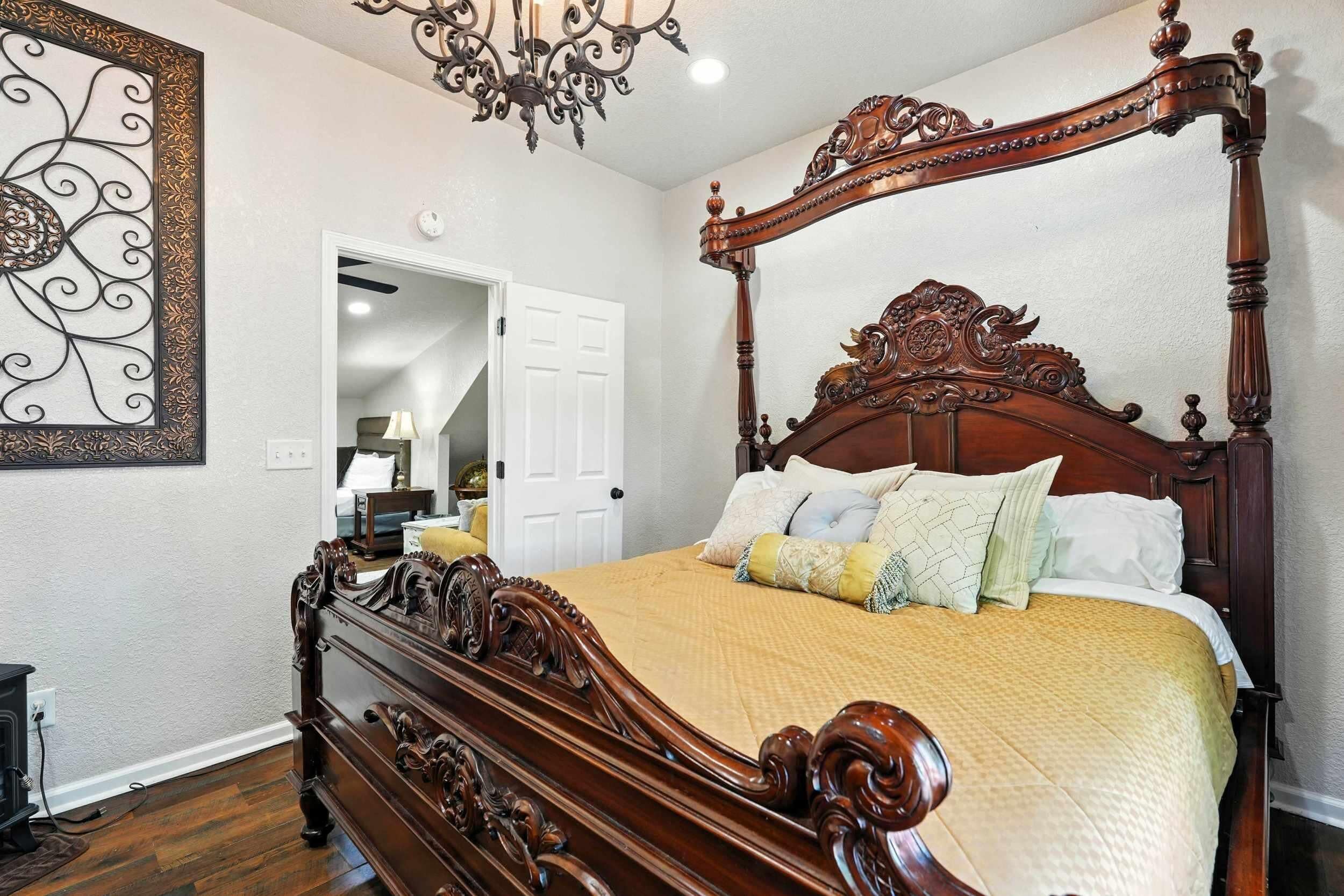 A bedroom with a four-poster bed, a chandelier, and a mirror on the wall.