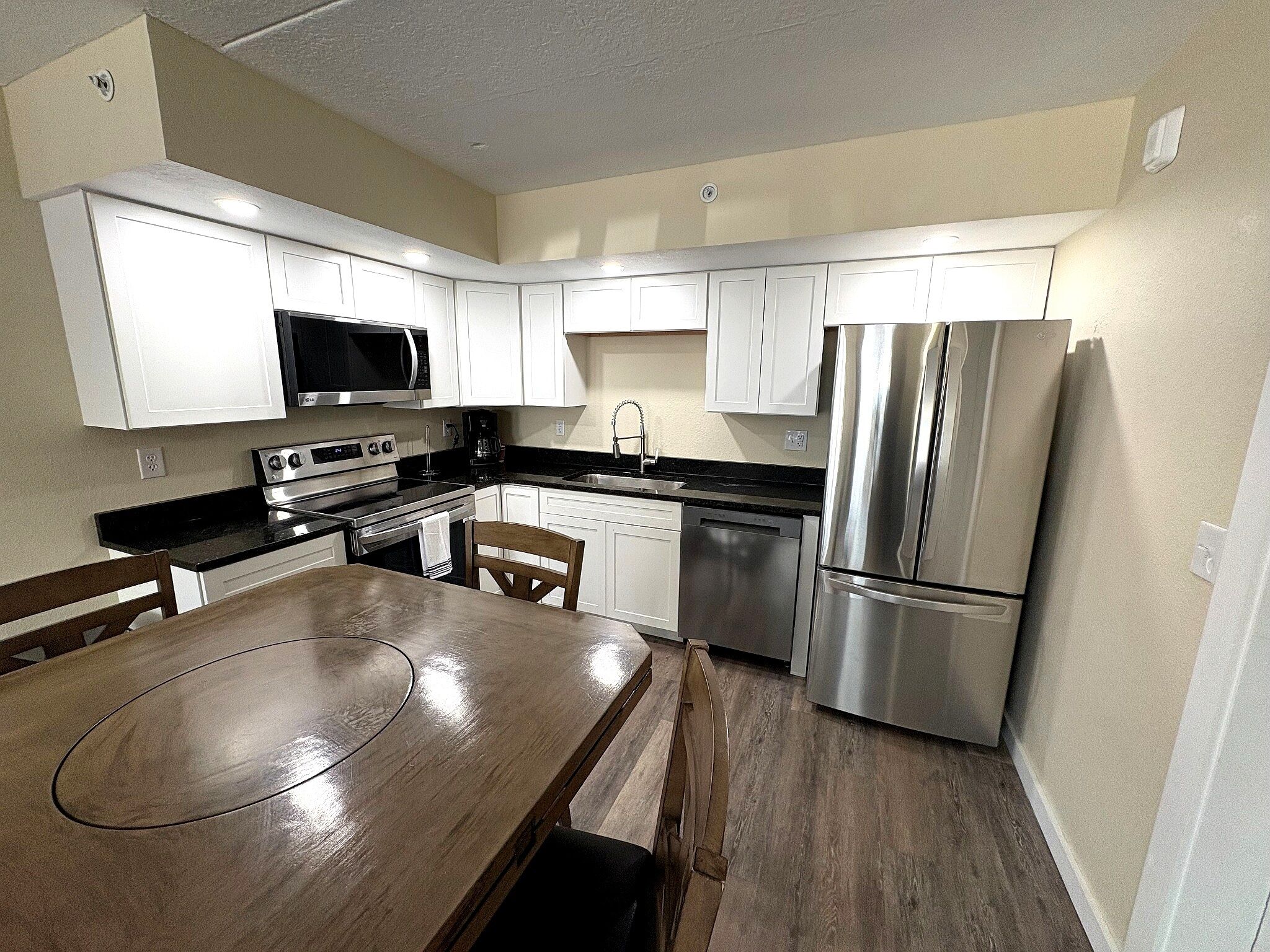 A kitchen with white cabinets, stainless steel appliances, a wooden dining table, and a dishwasher.