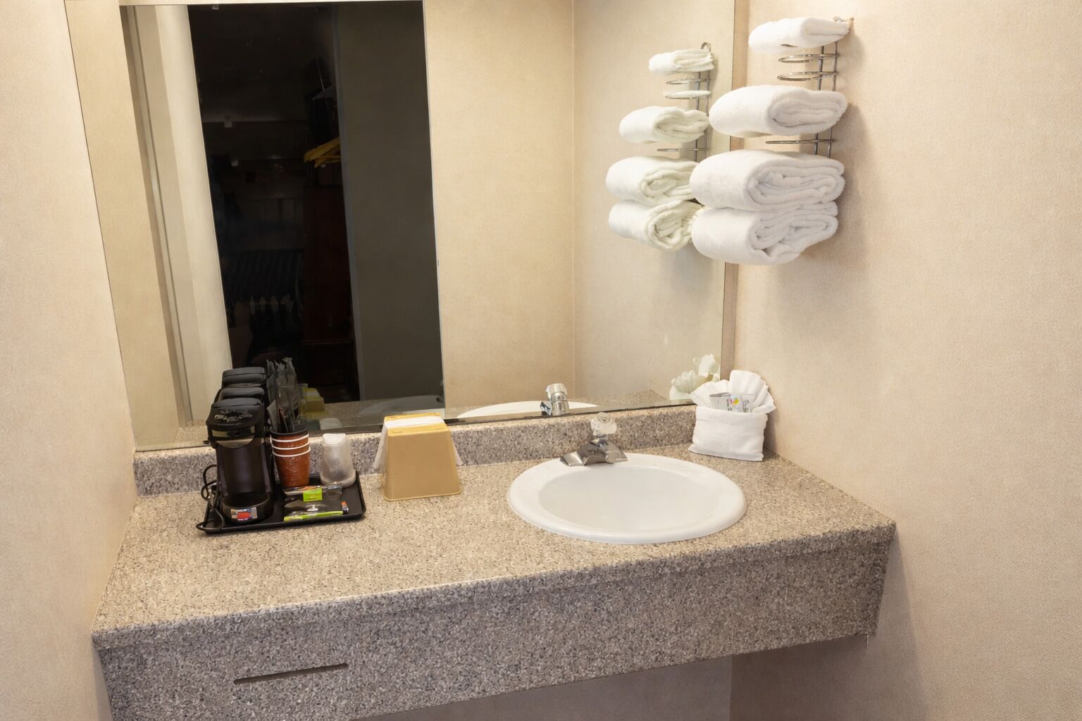 Une salle de bain d’hôtel avec un lavabo, une machine à café et des serviettes sur un porte-serviettes.