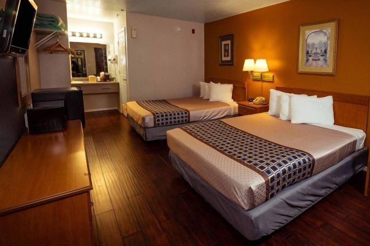 A hotel room with two beds, a desk, a chair, and a mirror.