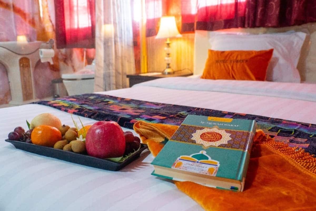 A neatly made bed with a colorful quilt, a tray of fruits, and a book on the side.