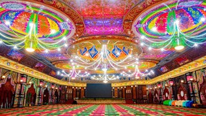 Un gran salón con decoraciones ornamentales en el techo, un amplio escenario central y una alfombra estampada.