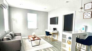 A modern living room with a grey sofa, a coffee table, a TV, and a desk with a chair. - ADU Washer and Dryer Kitchen Walk Bishop Arts (Dallas)