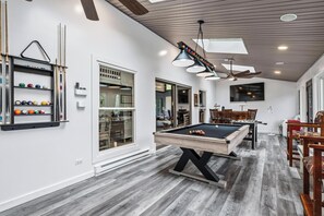A pool table with a modern design, a ceiling fan, and a billiards rack against the wall.