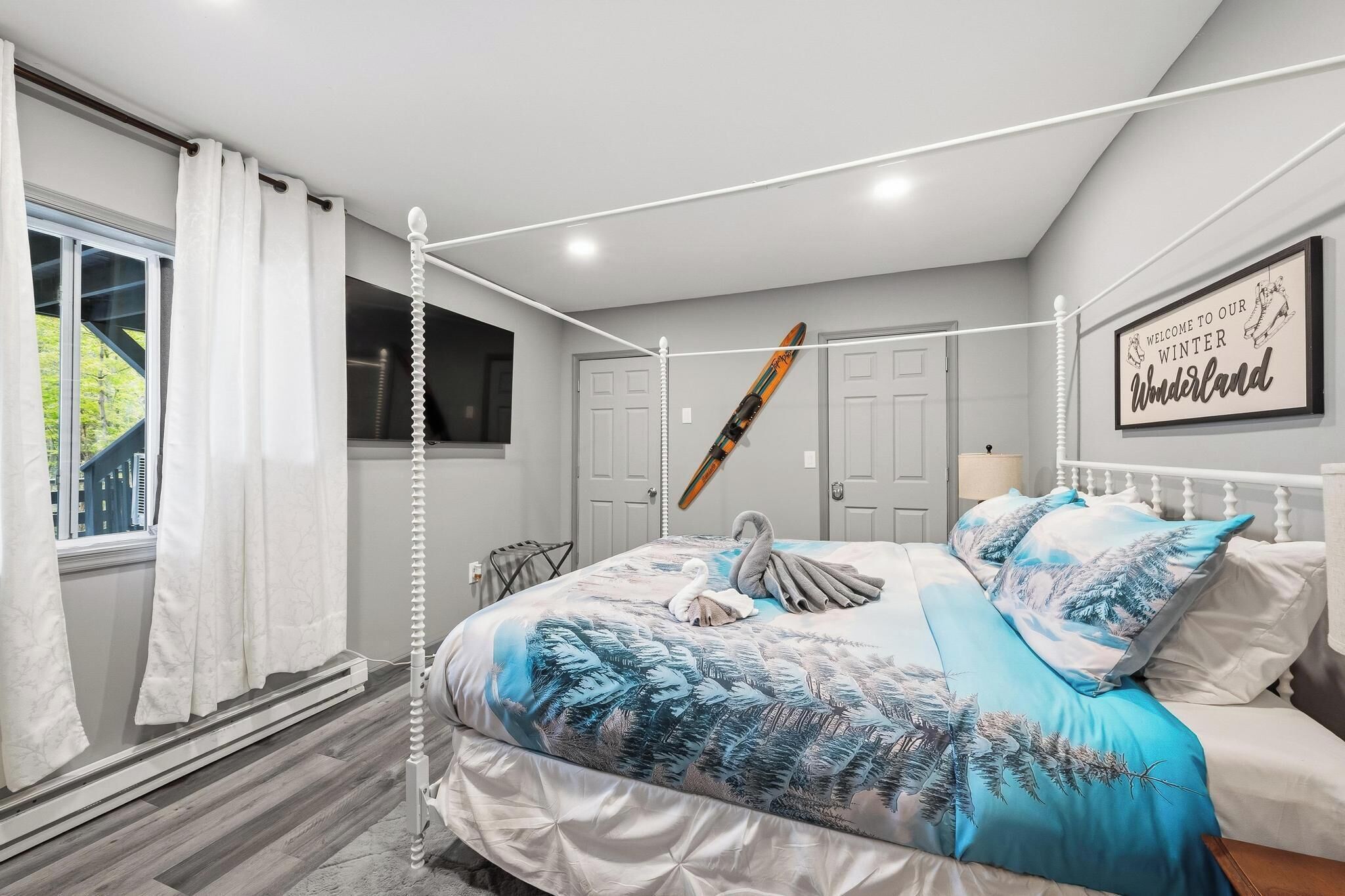 Une chambre à coucher avec un lit à baldaquin, une paire de skis accrochés au mur et une pancarte indiquant : « Bienvenue dans notre pays des merveilles hivernal ».