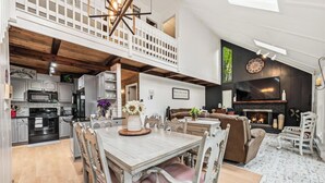 Amplio espacio tipo loft con una mesa de comedor, sillas, una chimenea y un televisor montado en la pared.