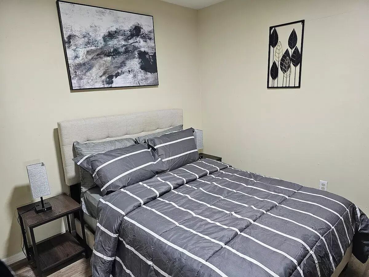 A neatly made bed with striped bedding, a bedside table with a lamp, and two wall-mounted artworks.