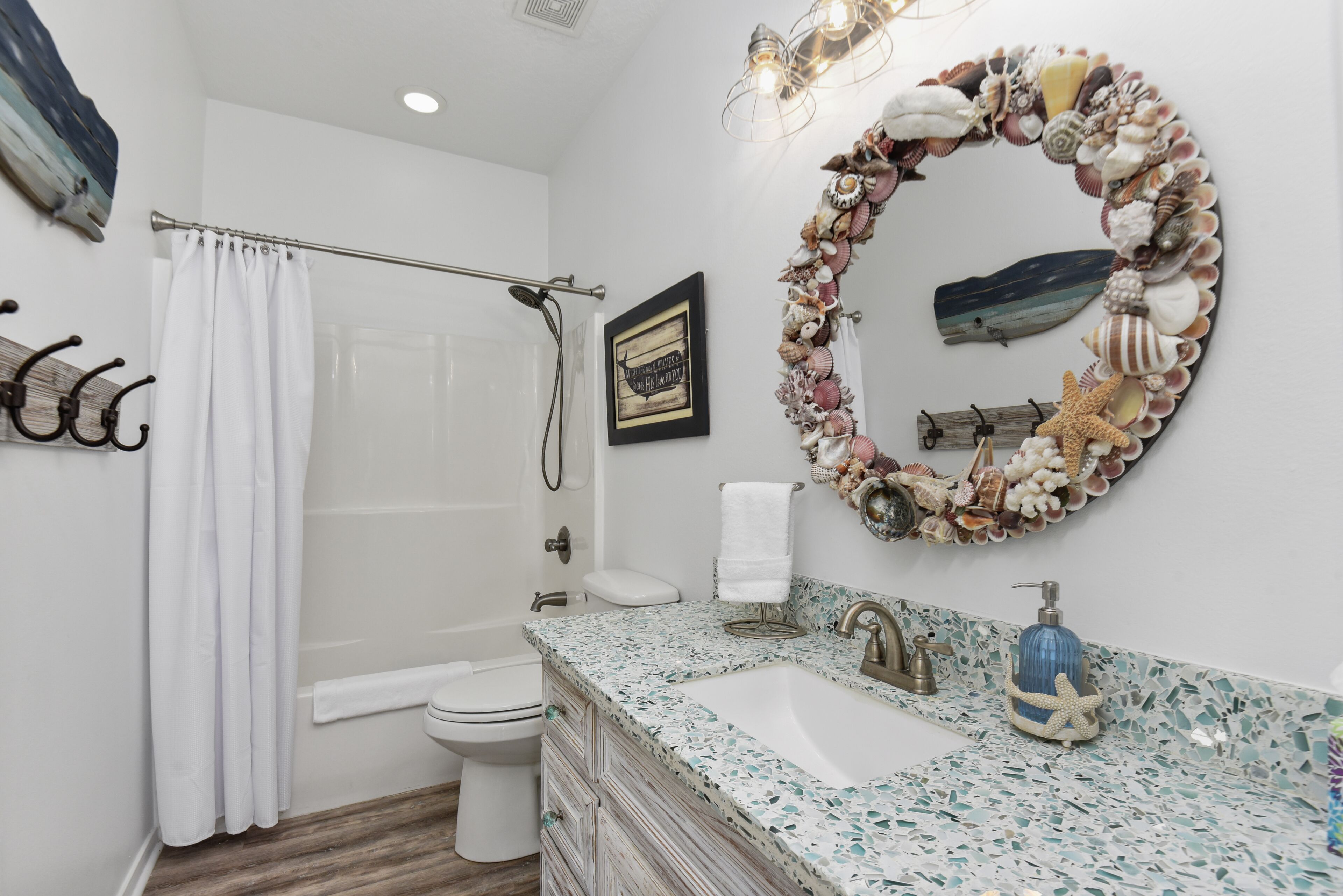 Une salle de bain équipée d’une douche, de toilettes, d’un lavabo et d’un mur décoratif orné de coquillages.