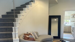 A modern living room with a curved grey sectional sofa, a round coffee table, and a staircase with white steps. - Stay in the top 2 floors of the brand new Silo Inn, near Zion!  (Washington)