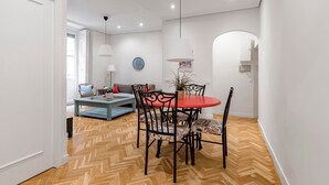 Una sala de estar moderna con comedor, que presenta piso de madera en patrón de espiga, una mesa redonda roja y un sofá con cojines estampados.