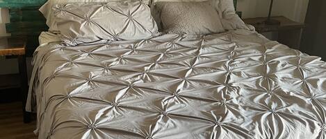 A bed with a tufted grey bedspread, a wooden headboard, and a bedside lamp.