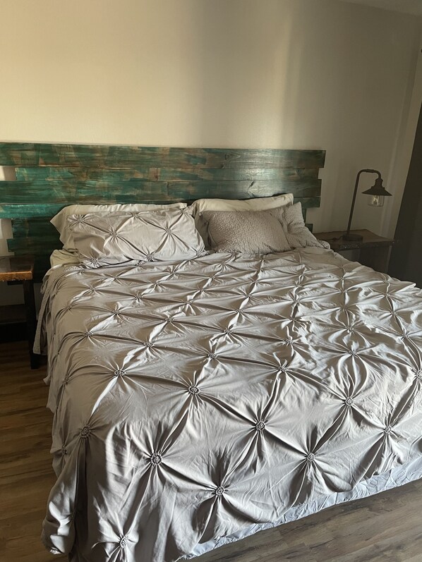 Una cama con colcha gris con textura, cabecera de madera y lámpara de noche.