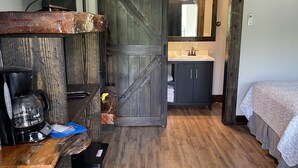 A room with a wooden floor, a bed, a desk with a coffee maker, a mirror, and a sliding door leading to a bathroom. - Black River Motel and Restaurant (Lesterville)