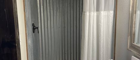 Een badkamer met een douche, betegelde vloer en een wastafel met toiletartikelen.