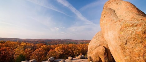 A large rock formation with a clear sky and autumn foliage in the background.
