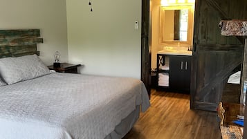 A bedroom with a bed, a ceiling fan, an air conditioning unit, wooden flooring, a nightstand, and a dresser.