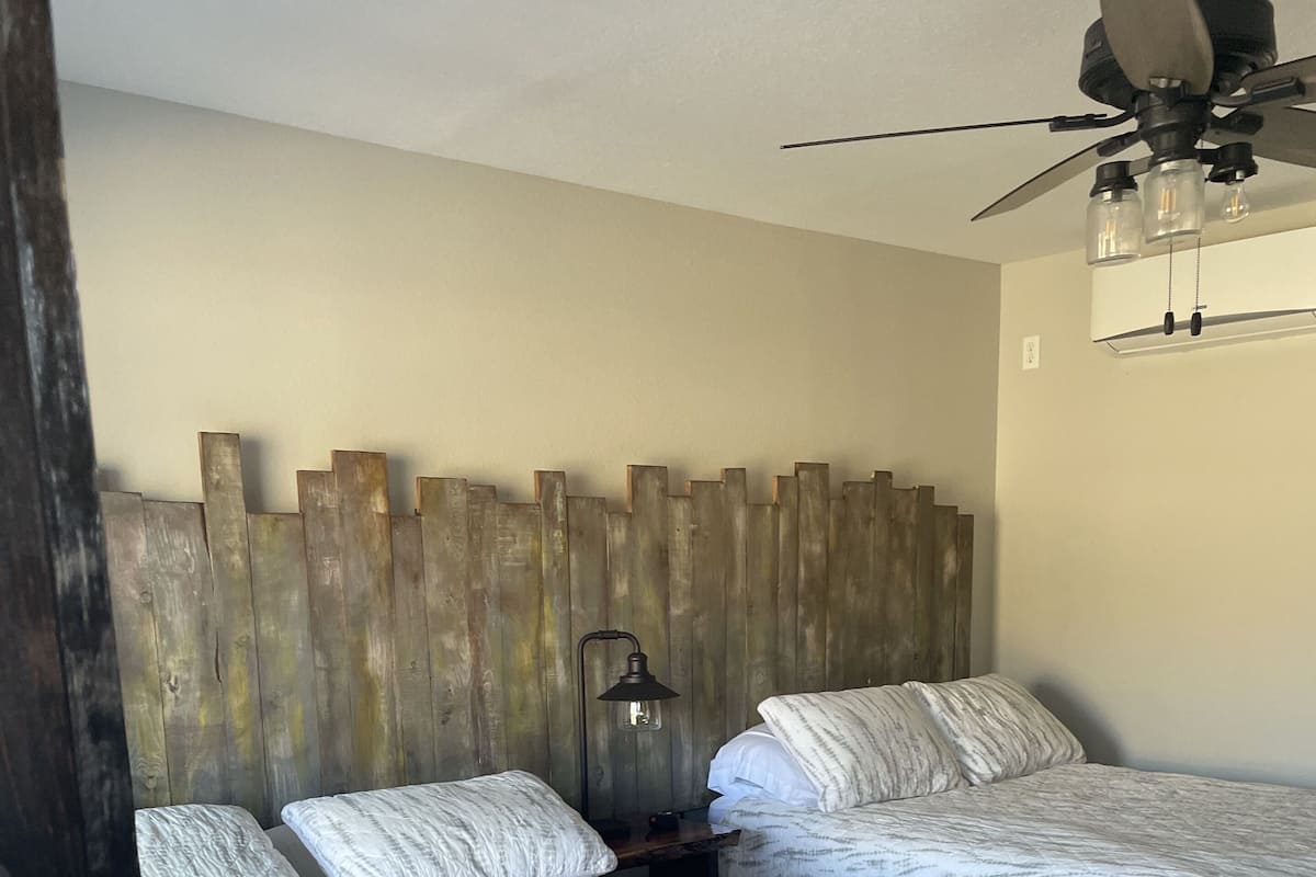 A bedroom with two beds, a wooden headboard, a ceiling fan, and a nightstand with a lamp.