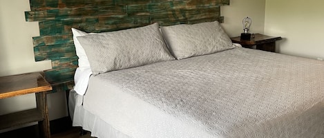 A bedroom with a wooden headboard, a bed with a white quilt, a nightstand, a wooden bench, and a ceiling fan.