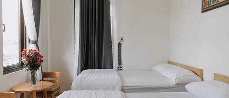 A hotel room with two beds, a wooden table with chairs, a vase of flowers, and a painting on the wall.