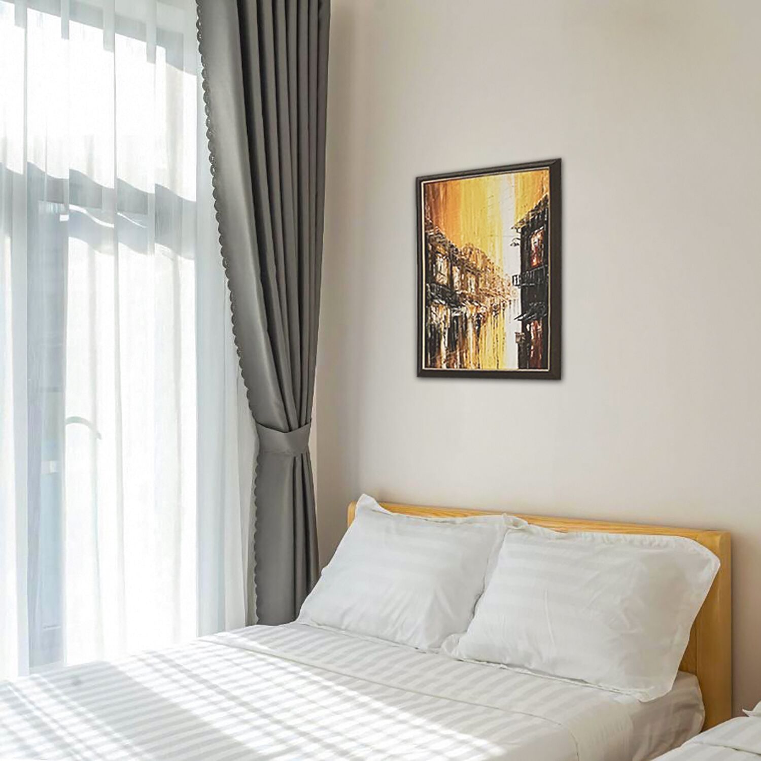 A hotel room with a bed, a painting on the wall, and a window with curtains.