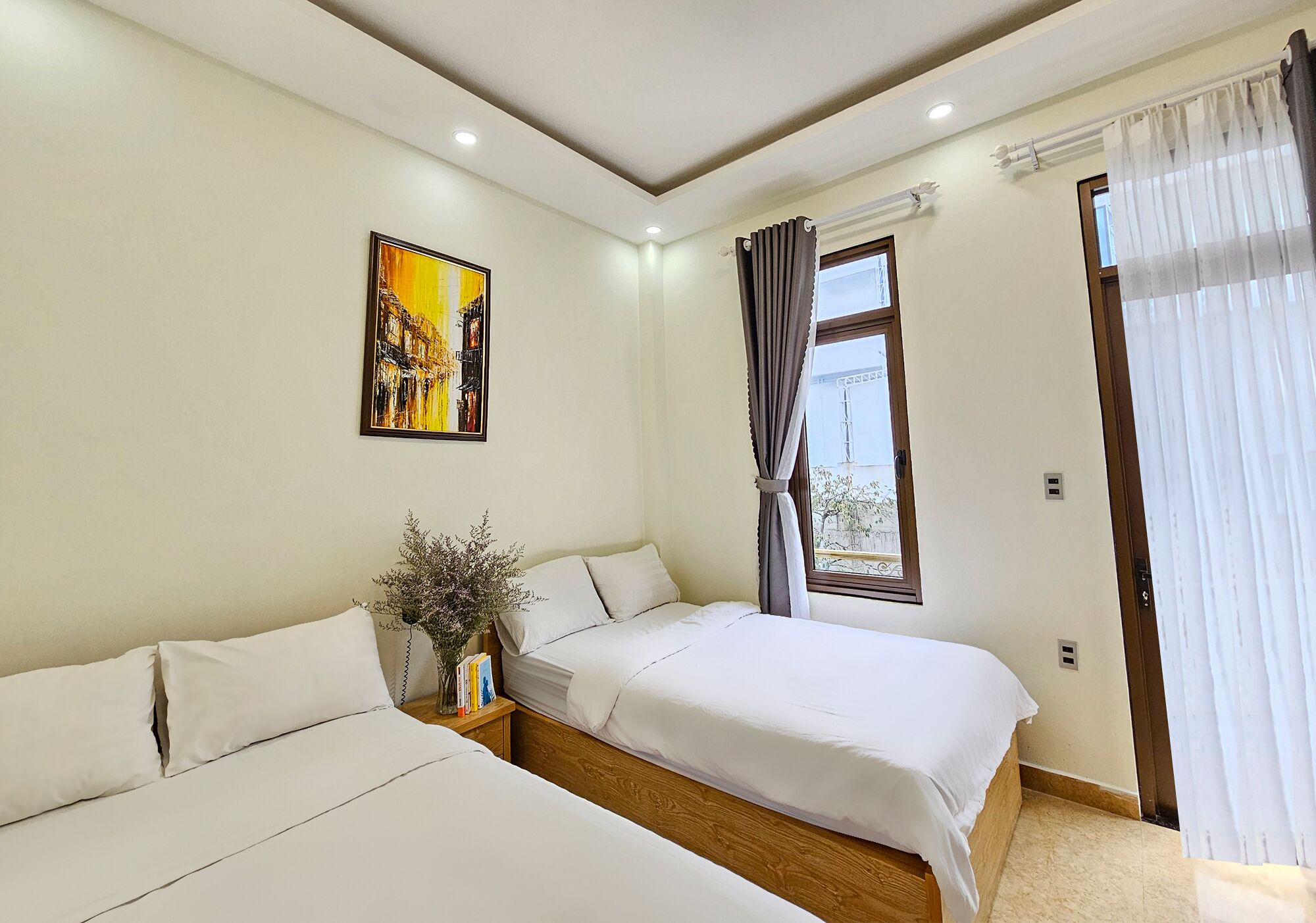 Una camera da letto con due letti, una finestra con tende, un quadro al muro e un comodino con un vaso.