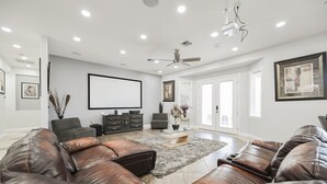 A spacious living room with leather sofas, a flat-screen TV, and a ceiling fan.