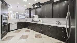A modern kitchen with dark cabinetry, stainless steel appliances, and a tiled floor.