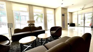 Un vestíbulo moderno con un sofá, sillas y una mesita. Amplias ventanas ofrecen luz natural y vistas al exterior.