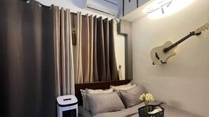 Un dormitorio con una cama, una guitarra colgada en la pared, un calentador y una cesta con flores.